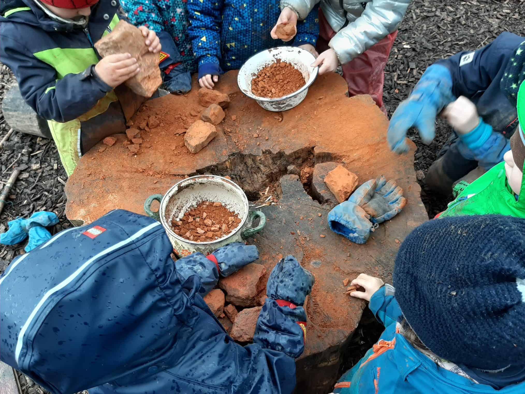 Zwei Kinder spielen an einer selbstgebauten Werkbank aus Paletten auf einer Wiese.
