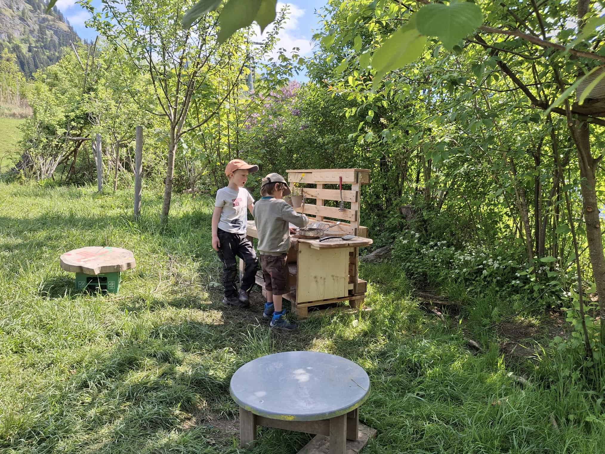 Zwei Kinder spielen an einer selbstgebauten Werkbank aus Paletten auf einer Wiese.