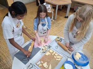 Kinder der OGS am BNG rollen Plätzchenteig aus um Osterhasenplätzchen zu backen.