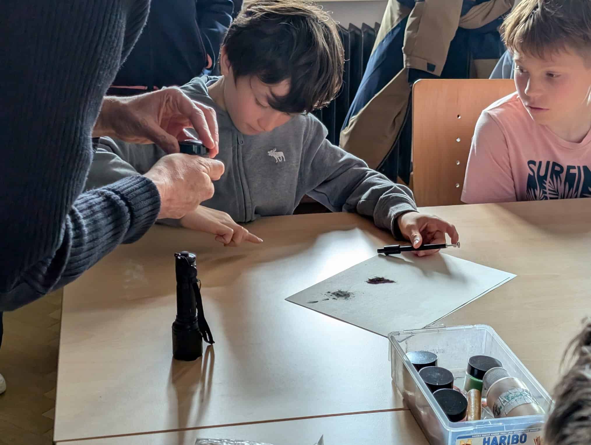 Ein Schüler sitzt an einem Tisch und probiert das Fingerabdruckpulver aus, das man bei der Spurensicherung verwendet.