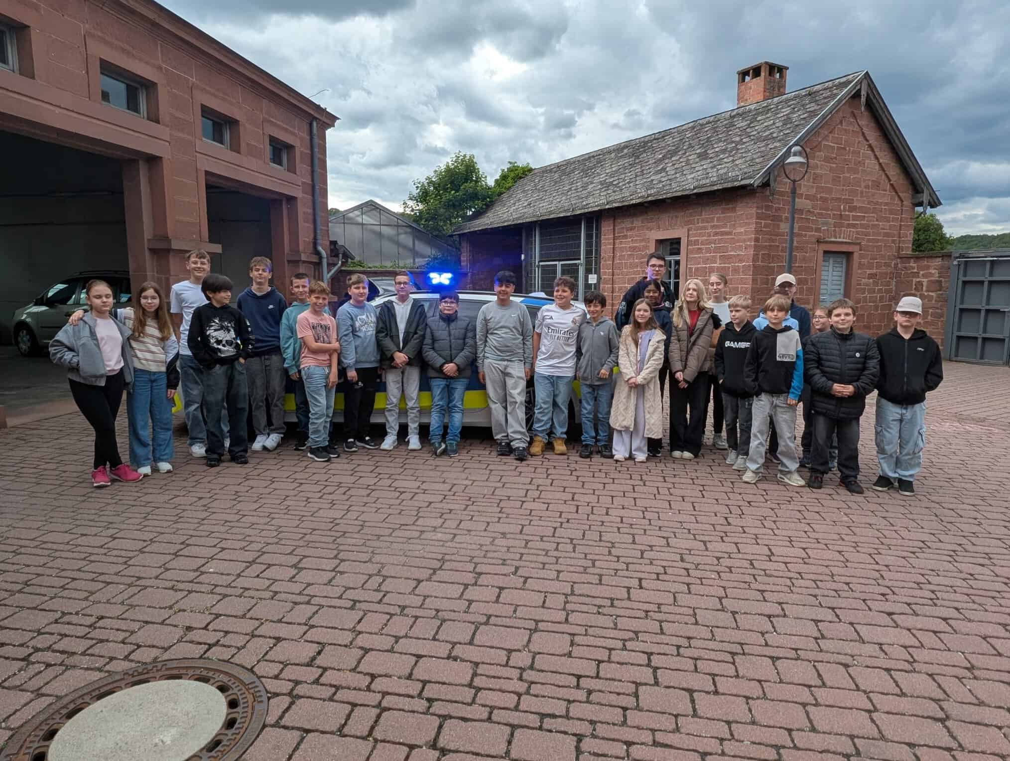 Die Schüler der OGS des BNG und der RSM stehen vor einem Polizeiwagen.