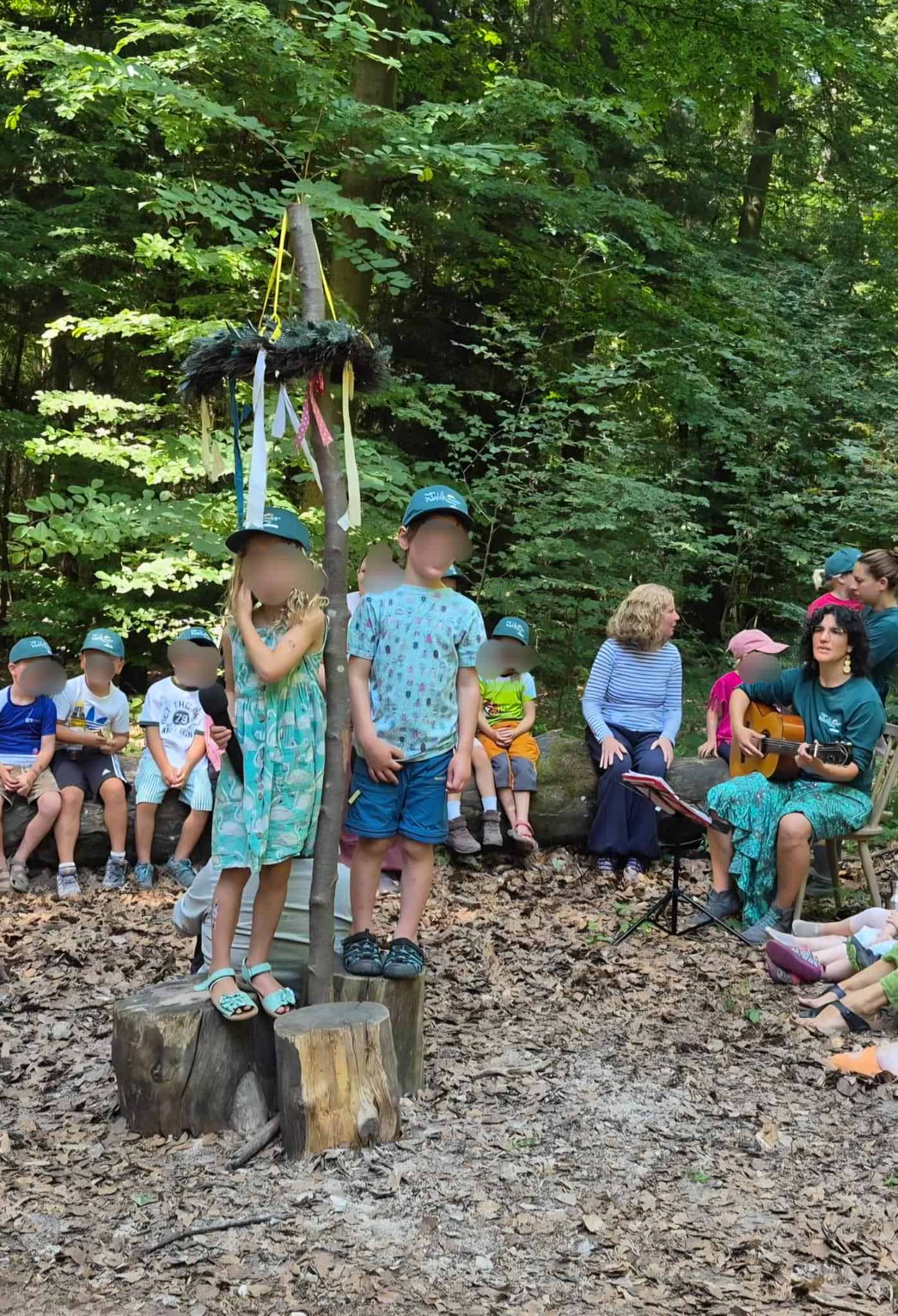 Die Kindergartenkinder sitzen mit den Erzieher:innen im Halbkreis und begrüßen die Gäste mit Liedern.